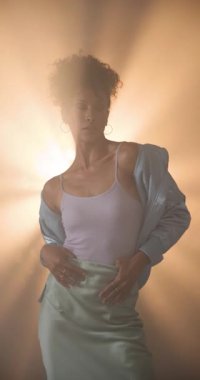 Dikey video: Parlak ceketli kadın saçlarını düzeltiyor, dramatik ışıklandırmada kendinden emin duruyor. Moda, güven, cazibe, tarz, kendine güvenen, zarafet