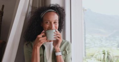 Pencere kenarında kahve içen bir kadın, düşünceli bir şekilde dışarı, eve bakıyor, fotokopi çekiyor. Düşünce, rahatlama, sabah, farkındalık, sıcaklık, dinginlik