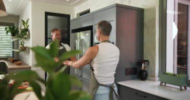 Beyaz adam, mutfak adasının yakınında sebze doğrarken beyaz kadının elini tutuyor ve dans ediyor. Romantizm, samimiyet, koreografi, sağlık, ev, bağlantı, neşe