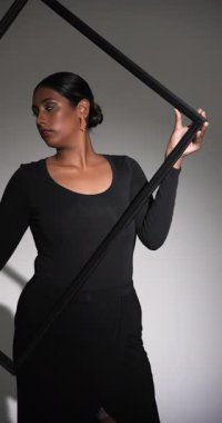 Dikey video: Modern moda stüdyosunda kendine güvenen siyah elbiseli bir kadın çerçeveyle poz veriyor. fotoğrafçı, cazibe, zarafet, portre, tarz, tasarımcı