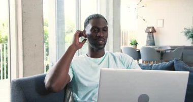 Modern oturma odasındaki kanepede oturan Afro-Amerikan bir adam, minderle gülümsüyor ve spor saati seyrediyor. Rahatlama, rahatlık, çağdaş, tarz, dekor, modern, sükunet