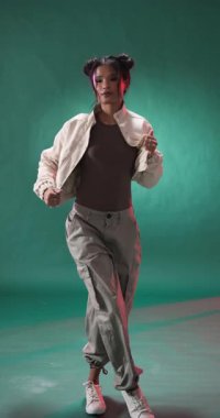 Dikey video: Şık grunge kıyafetli genç kadın stüdyo ortamında güven içinde poz veriyor. Moda, tarz, moda, model, alternatif