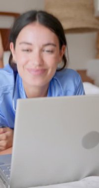 Dikey video: Yatak odasında çalışırken dizüstü bilgisayara odaklanan genç bir kadın. Teknoloji, konsantrasyon, yaşam tarzı, seyahat, çalışma alanı, odaklanma.