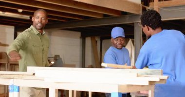 Afro-Amerikan erkek ustabaşı el rehberliği ekibini kaldırarak atölyedeki tabletlerle kalasları hizaladı. İnşaat, takım çalışması, ahşap işçiliği, endüstriyel, el işi, işçilik, organizasyonel