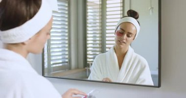 Saç bandı takan ve lavaboda su içmesi için göz altı bantlarına masaj yapan bir kadın. Cilt bakımı, güzellik, kendine dikkat, rahatlama, sağlık, ayna, şımartma.