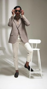 Dikey video: Modern moda stüdyosunda kendine güvenen güneş gözlüklü şık bir adam. Moda, trend, kentsel, erkek, modellik