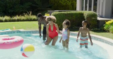 Havuzda Afrika kökenli Amerikalı ebeveynler, top toplayan anne ve babalar atarken çocuklar su sıçratıyor. Aile, eğlence, açık hava, eğlence, neşeli, hayat dolu, yaşam tarzı.