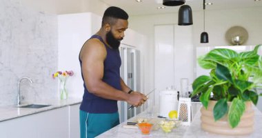 Modern mutfakta bıçak ve kâseyle mermer tezgahta sebze doğrayan Afro-Amerikalı bir adam. Yemek pişirme, hazırlık, aşçılık, sağlıklı, modern, mutfak gereçleri, odaklanma.