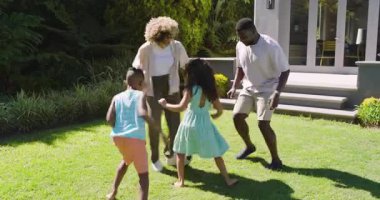 Çeşitli aileler çimenlerde futbol oynuyor, baba topu yerleştiriyor, kız salya akıtıyor, anne çocuğa yardım ediyor. Açık hava, eğlence, aktivite, neşeli, rahat, enerjik, bağ kurma