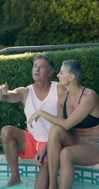 Dikey video: Havuzda dinlenme, sabah güneşinin ve sohbetin tadını çıkaran olgun çift. Havuz başı, rahatlama, açık hava, boş zaman, tatil, yaşam tarzı.