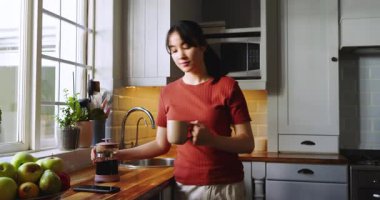 Mutfakta kahve makinesiyle kahve doldurmak, Asyalı kadının yudumlaması, kaydırmalı akıllı telefon bildirimi. Minimalist, rahat, yaşam tarzı, çağdaş, sıcak, doğal, sakin