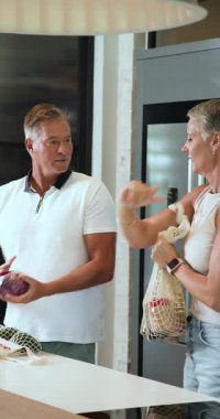 Dikey video: Mutfakta olgun bir çift taze ürün seçiyor ve birlikte yemek pişirmekten zevk alıyor. ev hayatı, sağlıklı beslenme, aşçılık, ilişki, ortaklık, sebzeler