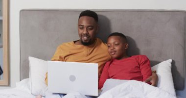 Baba ve oğul laptopta bağ kurmak için uygulama açıyor, yatakta heyecan verici içerikler izliyorlar. Aile, bağ, rahatlama, ev, samimiyet, birliktelik, sıcaklık.