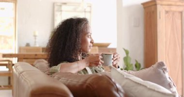 Kadın kanepede dinleniyor, kahvenin tadını çıkarıyor ve evde sıcacık gülümsüyor. Rahatlık, rahatlık, rahatlık, rahatlık, ev, yaşam tarzı.