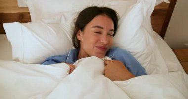 Yatakta mavi pijamalı bir kadın sabah evde neşeyle gülümsüyor. Rahatlık, rahatlama, mutluluk, sabah rutini, gündelik, yaşam tarzı