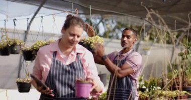 Bahçe merkezi önlüklü çeşitli işçiler serada dijital tablet kullanırken bitkileri tartışıyor. Bahçıvanlık, bahçıvanlık, takım çalışması, teknoloji, perakende, işbirliği