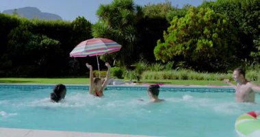 Havuz kenarında el ele tutuşan farklı arkadaşlar suya atlıyor ve eğlence için sallanan çörekler yüzüyor. Sıçrama, neşe, rahatlama, arkadaşlık, rahatlık, yaz, coşku