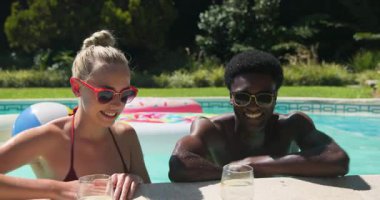 Çeşitli arkadaşlar havuz başında kadeh kaldırırken bir kadın içkiye uzanıyor, yudumluyor ve yakınlaşıyor. Rahatlama, rahatlama, yaz, açık hava, canlı, çiftler, yaşam tarzı.