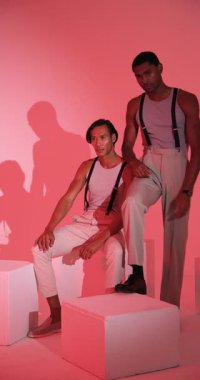 Dikey video: Askılı iki şık adam modern moda stüdyosunda güven içinde poz veriyor. stil, giyim, erkek modası, mankenlik, moda