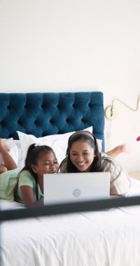 Dikey video: Anne ve kızı rahat bir yatakta dizüstü bilgisayarda sinemadan keyif alıyorlar. Aile, bağ, rahatlama, rahatlama, teknoloji, eğlence