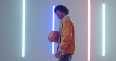 Neon ışıklı stüdyoya giriyoruz, Afrikalı Amerikalı adam ritim ve gösteri kontrolünü sağlamak için basketbol oynuyor. Moda, spor, performans, minimalizm, canlı, hareketli, kentsel