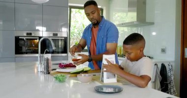 Kaşık toplama, Afrika kökenli Amerikalı baba ve oğlu peynir rendeleme tezgahta pizza için sos yayma. Aile, yemek pişirme, mutfak, bağ kurma, takım çalışması, ev işleri.