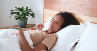 Kadın yatakta dinleniyor, gülümsüyor ve sabah rahatlığının tadını çıkarıyor, evde. Rahatlama, rahatlama, yaşam tarzı, mutluluk, yatak odası, pozitiflik.