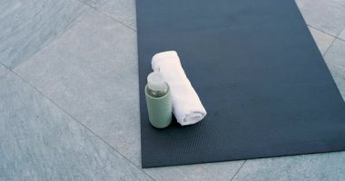 Camera is initiating panning, tilting and revealing towel, water bottle on mat on terrace floor. Fitness, wellness, meditation, exercise, outdoor, minimalist, relaxation