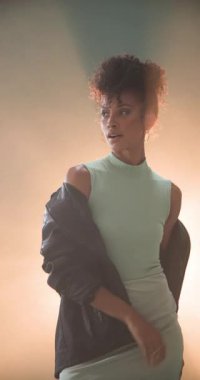 Dikey video: Deri ceketi ayarlayan kendine güvenen bir kadın, stüdyo aydınlatmasında gergin bir tarzı benimsiyor. Moda, güven, giysi, portre, cesaret