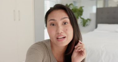 Yetişkin bir Asyalı kadının kamerayı selamlaması yatak odasından başlayıp mesajını paylaşması. İçerik yaratan, gündelik moda, rahat iç mekan, yaşam tarzı, iletişim, otantik, rahat