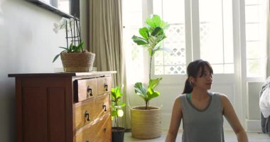 Duruşunu ayarlıyor, yoga minderinde oturan Asyalı kadın güneşli odada nefes alıp veriyor. Farkındalık, sağlık, meditasyon, dinginlik, rahatlama, doğal ışık, sakinlik