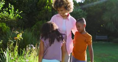 Bahçede koştuktan sonra kucaklaşan, çiçek toplayan ve taç yapraklarını açıklayan Afrikalı Amerikalı anneler. Aile, yetiştirme, açık hava, doğa, bağlanma, eğitim, eğlence