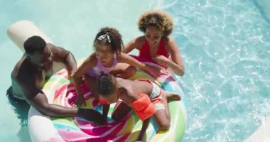 Babamın itişinden sonra farklı ailelerin donat ve kollarıyla havuzda dengede durması. Aile, su, eğlence, canlı, birliktelik, neşeli, yaz