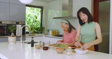 Çinli bir anne, kızına yemek için tabak koyarken mutfak adasında soğan doğramayı öğretiyor. Aşçılık, işbirliği, aile, gelenek, mutfak, ev hayatı