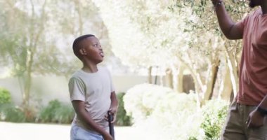 Afrikalı Amerikalı baba, oğlunun arka bahçedeki yeşil alanda golf sopasıyla atış talimi yaptığını ve isabetini artırdığını söylüyor. Aile, akıl hocalığı, açık hava, eğlence, koçluk, boş zaman, yetenek geliştirme.