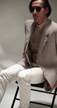 Dikey video: Modern moda stüdyosunda kendine güvenen güneş gözlüklü şık bir adam. stil, özgüven, göz giyimi, moda, çağdaş