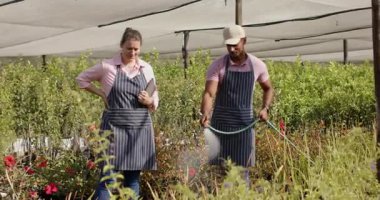 Çocuk bahçesinde çiçekleri sulayan bir adam ve tabletli bir kadın serada gözlemliyor. Bahçıvanlık, bahçıvanlık, takım çalışması, teknoloji, tarım, işbirliği