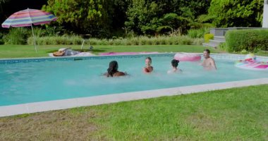 Çeşitli arkadaşlar arka bahçedeki havuza girip yüzerek ve topu yakalayarak suya atlıyorlar. Boş zaman, eğlence, rahatlama, canlı, açık hava, sosyal, aktivite