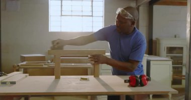 Bankın çerçevesini yerleştirdikten sonra, yetişkin bir Afro-Amerikan marangoz dükkanında zımparalanmış, kopyalama alanı. Sanatçılık, marangozluk, zanaatkarlık, doğal ışık, odaklanma, diy, iç mekan