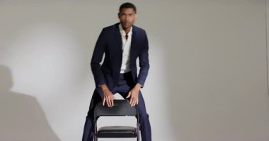 Sandalyeye uzanmış, takım elbiseli Afro-Amerikan bir adam oturmuş, çenesini dinlendirip, fotoşopa bakıyor. Profesyonel, portre, minimalist, moda, zarafet, sofistike, stil