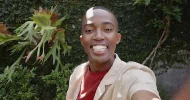 Bahçe manzarasını telefonla paylaşan bir adam gülüyor, sarmaşık duvarını işaret ediyor. Doğa, yeşillik, açık hava, yaşam tarzı, gündelik, canlı, anlamlı