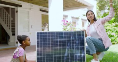 Anne ve kızı güneşli arka bahçede güneş paneli teknolojisini araştırıyor. Yenilenebilir enerji, sürdürülebilirlik, güneş enerjisi, çeşitli aileler, çevre