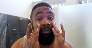 Afro-Amerikalı bir adam parlak modern banyoya yüz kremiyle cilt kremi sürüyor. Tımar, cilt bakımı, banyo, modern, kişisel bakım, minimalist