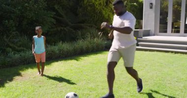 Farklı baba ve oğul top sürme pratiği yaparken, baba da antrenman için çimlerde yuvarlanıyor. Aile, akıl hocalığı, açık hava aktivitesi, atletizm, koçluk, boş zaman, çocukluk.