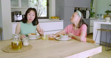 Çinli anne ve kız mutfakta durup çay içerek telefonda kaynaşma gösteriyorlar. Aile, bağ, gelenek, sıcaklık, mutfak, iletişim, modern