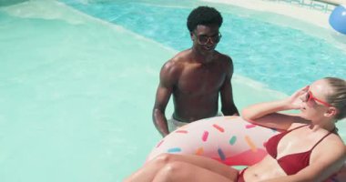 Bahçe havuzunda dinlenen, mayo giymiş çeşitli çiftler, yüzen donut ve sürüklenen kadınlara rehberlik eden erkekler. Boş zaman, romantizm, yaz, su, tropik, sükunet, dinlenme