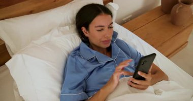 Pijamalı bir kadın yatakta uyanıyor, esniyor ve güne evde başlıyor. Günaydın, uyan, rutin, rahatla, rahat, yatak odası.