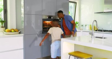 Afro-Amerikalı baba ve oğul fırını açıyor, fırını alıyor ve yemek tabaklarını paylaşıyorlar. Aile, yemek pişirme, kaynaşma, modern, sade, hazırlık, mutfak