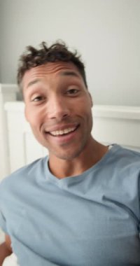 Dikey video: Gülümseyen adam evde rahat rahat mavi gömleğini giyiyor, keyfine bakıyor. Rahatlama, yaşam tarzı, konforlu, mutluluk, giysi, kapalı alan