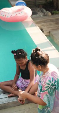 Dikey video: Anne ve kızı havuzda dinleniyor, güneşli bir öğleden sonranın keyfini çıkarıyorlar. Aile, bağ, açık hava, boş zaman, yaz, tatil